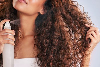 Woman sprays curl refresher on her curly hair.