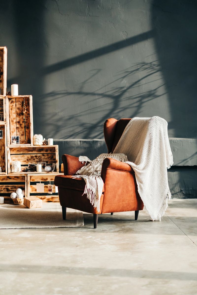 Interior of living room with big armchair and decorative wooden boxes in sunlight.