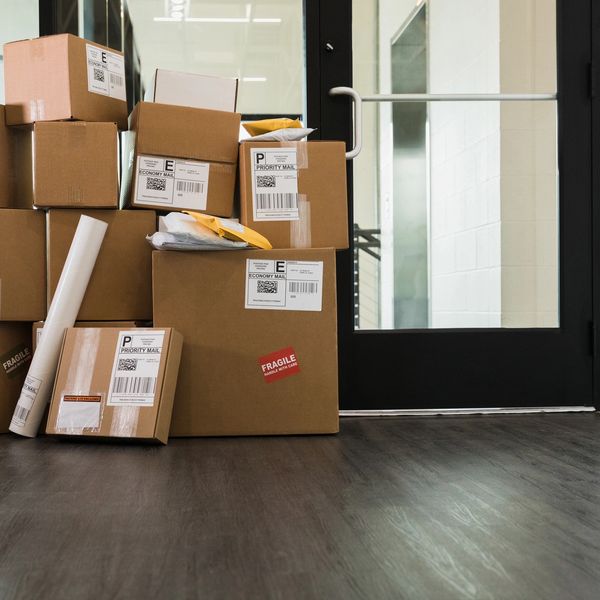 Stack of various cardboard packages and mail near a glass door indoors.