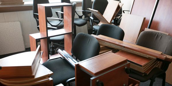 Disassembled furniture and office chairs clutter a room near a window.