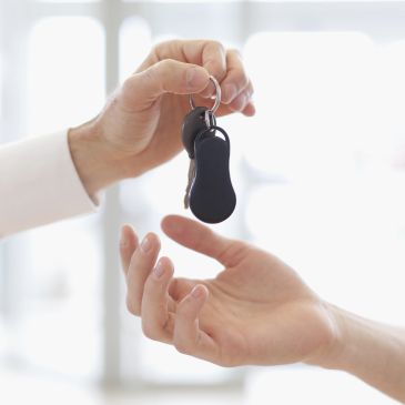 One person handing car keys to another indoors.
