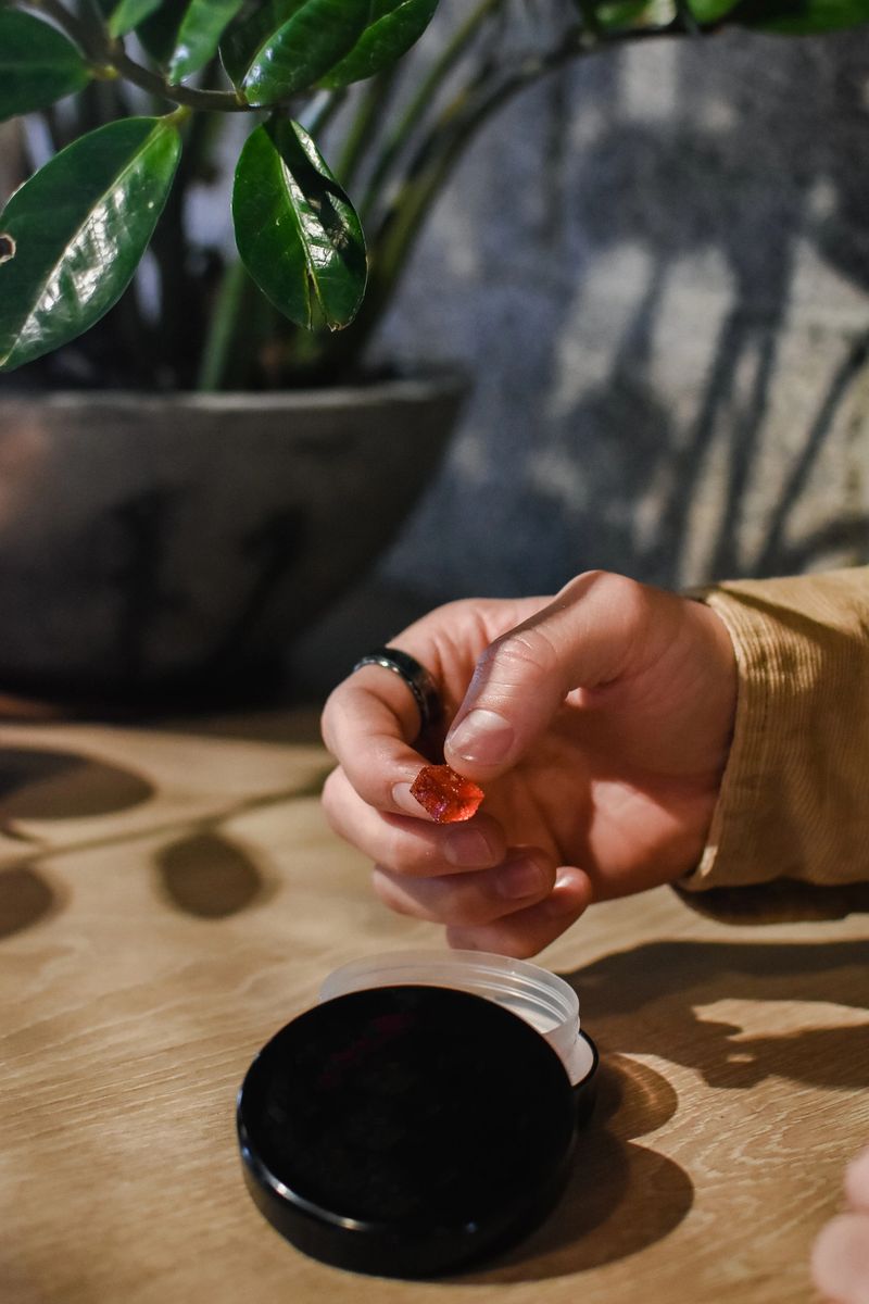 A young man holding a red gummy with a black canister next to him