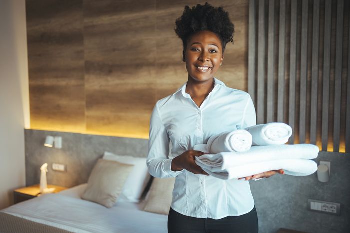 Smiling hotel staff holding clean towels in a cozy room.