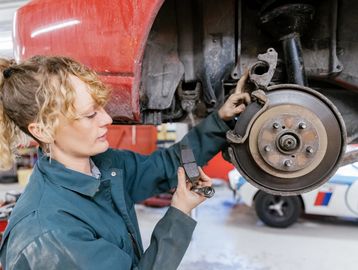 Woman repairing car brakes in a garage.