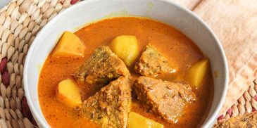 A bowl of spicy fish curry with potatoes in rich orange sauce.