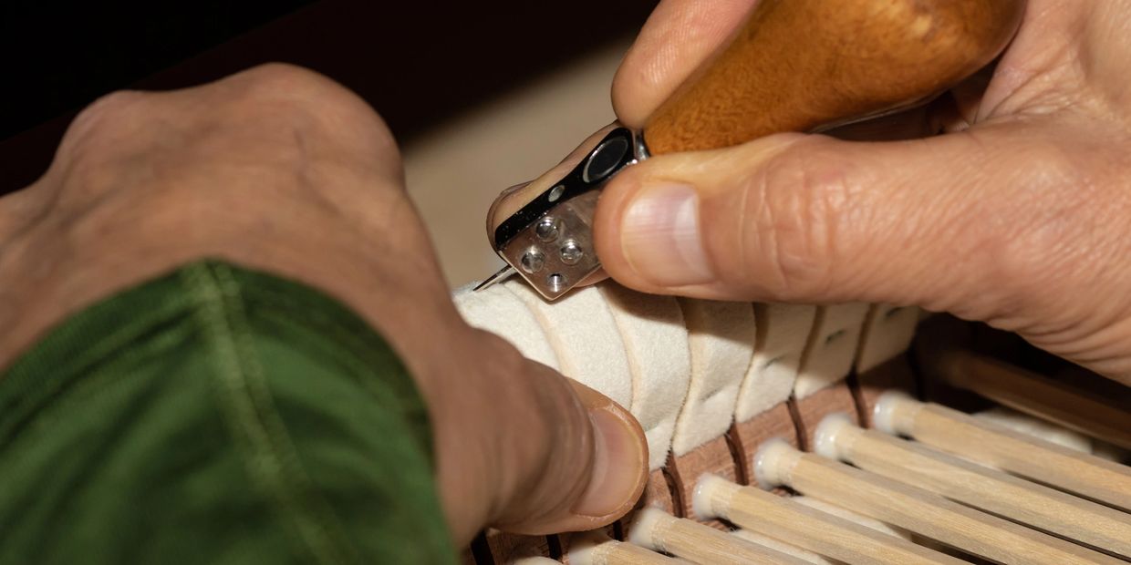 Close-up of hands working on piano hammer felt with a tool.