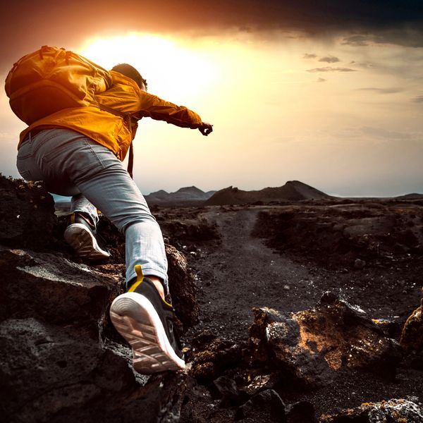 Person climbing rocky terrain towards the sunset.
