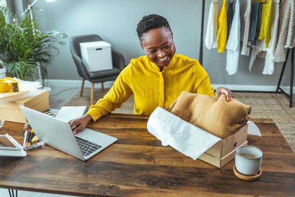 Woman happily unboxing a fabric item while using a laptop for a online dropshipping store.