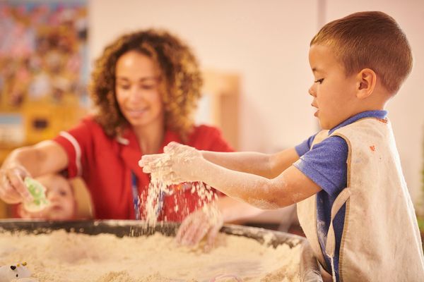 Child playing with sand while adult watches.
