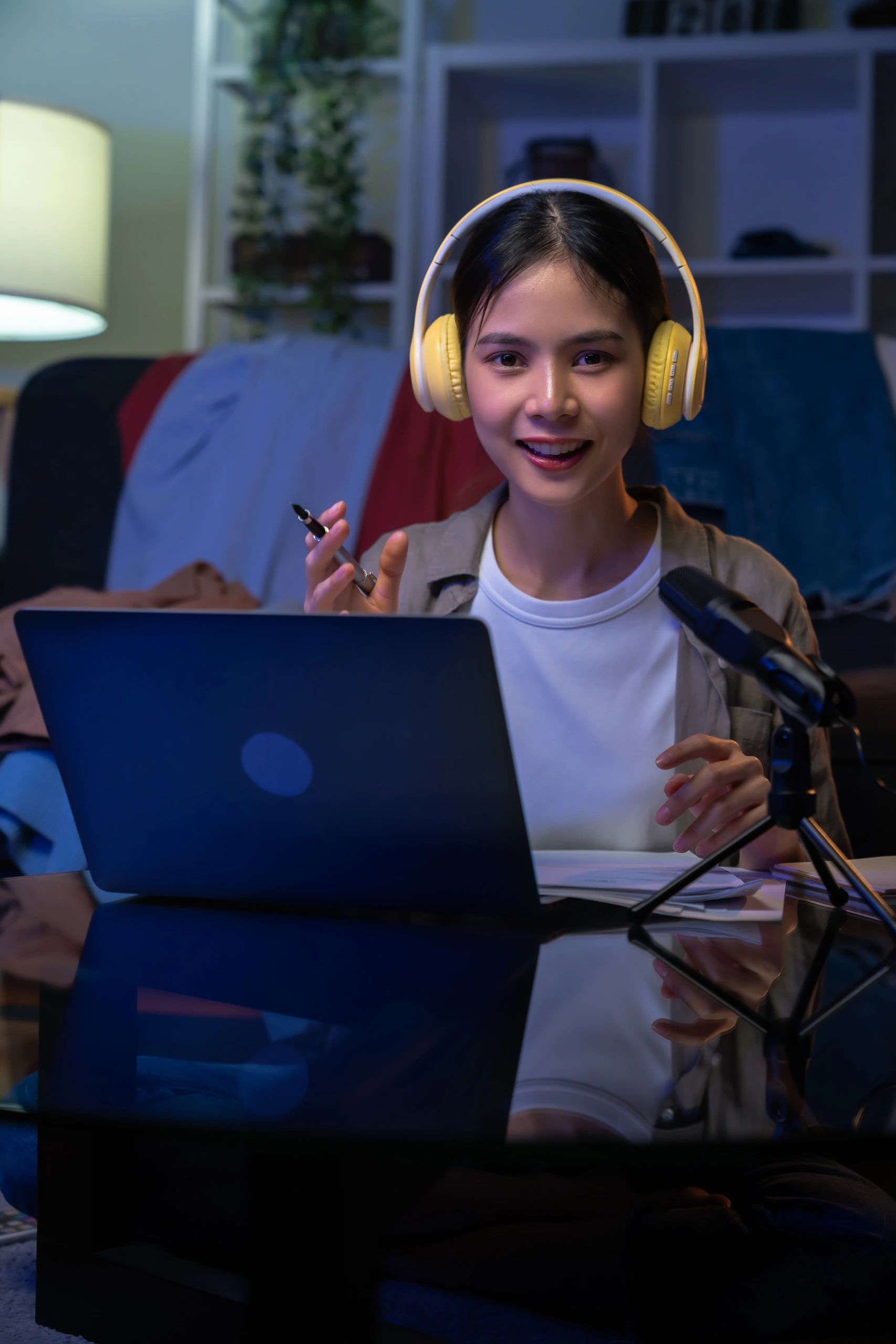 Young woman speaking with yellow headphones in front of a laptop.