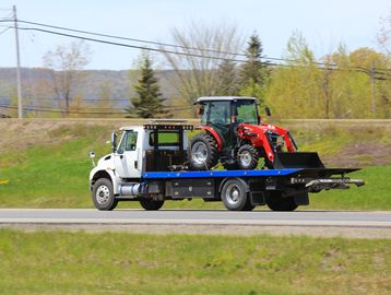 Flatbed truck carrying a red tractor on a road.