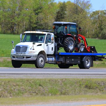 White flatbed truck transporting a red tractor on a rural road.