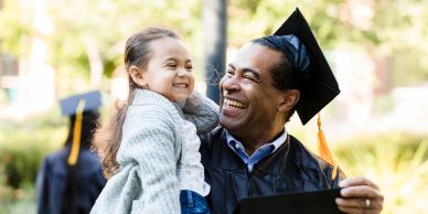 Graduate joyfully holding a young child outdoors.
