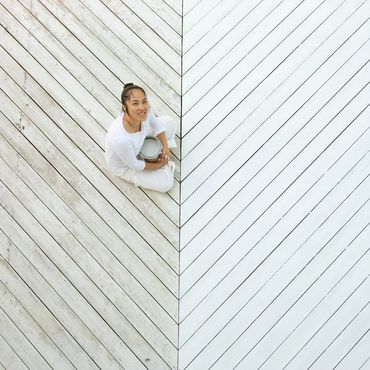 Woman sitting on a wooden floor holding a paint can, half-painted white.