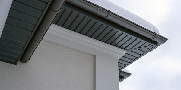 Snow-covered roof gutter on a modern house with white walls.