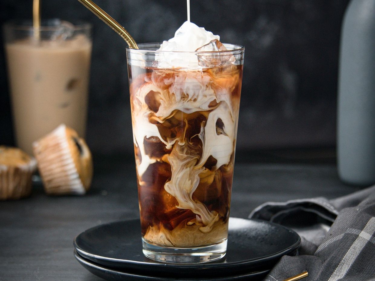 Iced coffee with cream swirling and whipped topping in a glass.