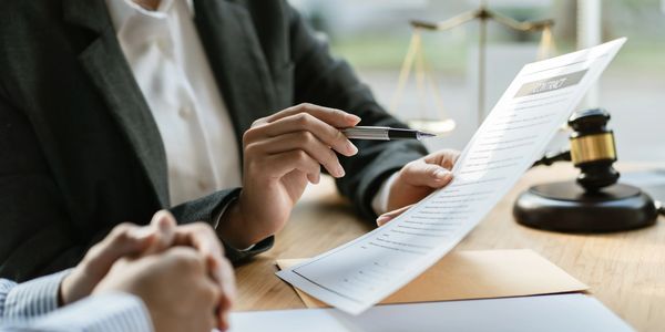 Person reviewing a contract document with a pen, legal scales, and gavel nearby.