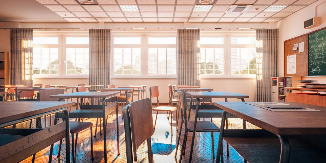 Sunlit empty classroom with wooden desks and chairs.