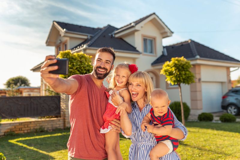 Beautiful happy family having fun taking selfie using smart phone in front of their new house