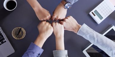Four people doing a fist bump over a desk.