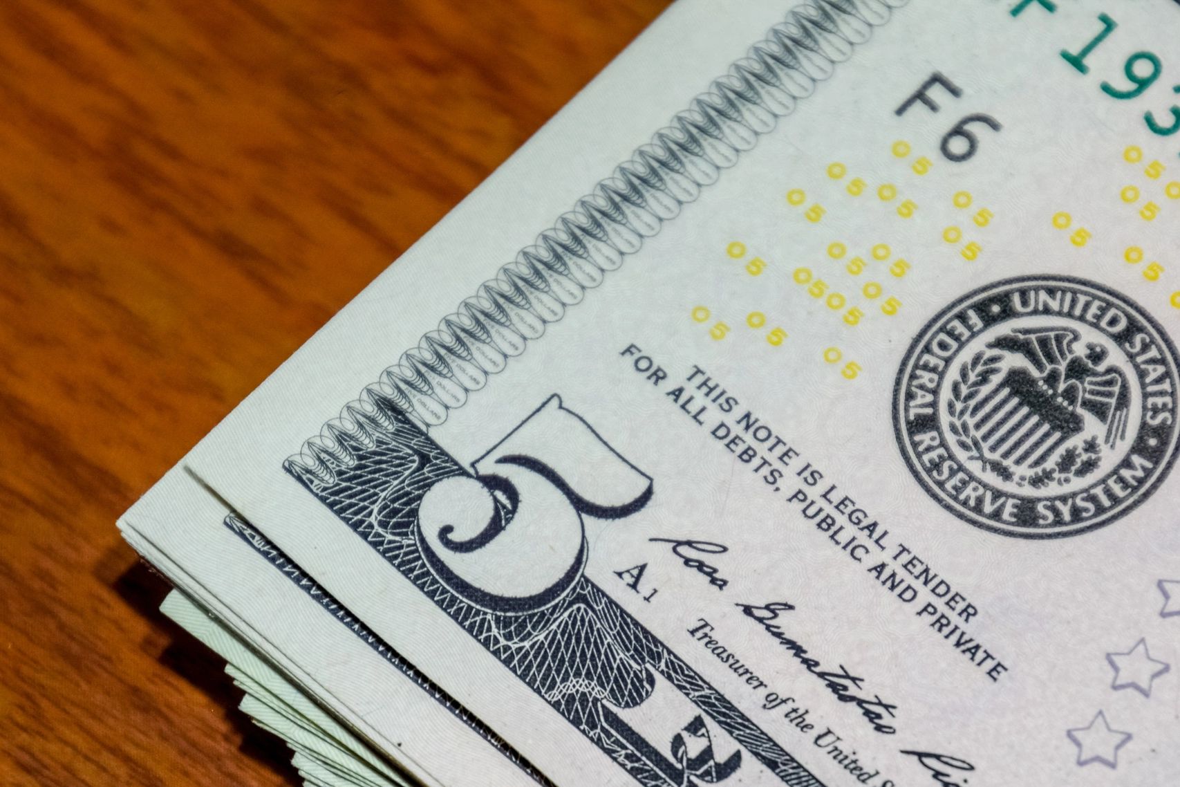 Close-up of folded five-dollar bills on a wooden surface.