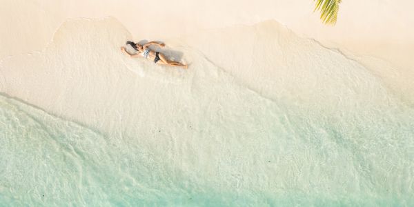 A person relaxing on a serene beach with clear blue water and white sand.