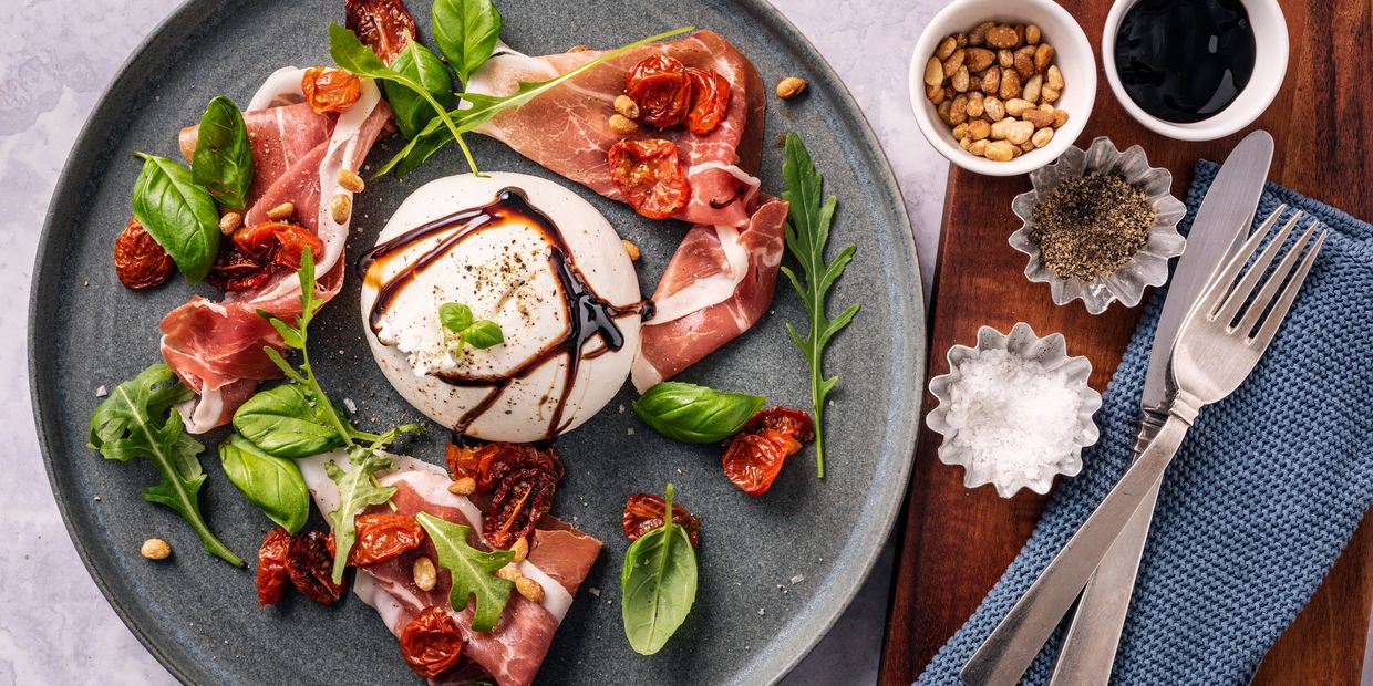 Gourmet burrata with prosciutto, sun-dried tomatoes, basil, and balsamic glaze.