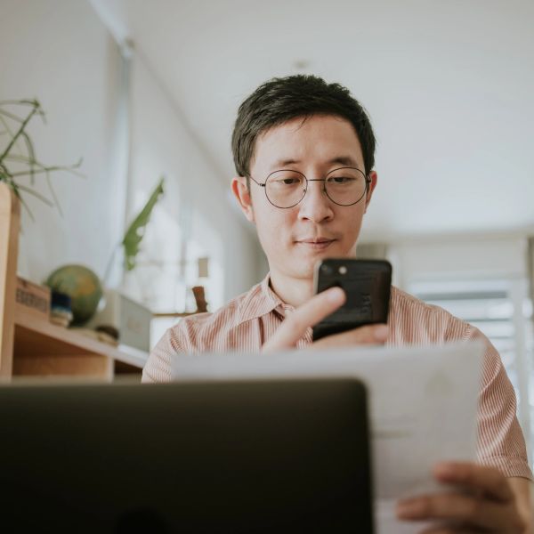 Man using phone and reading paper in home office.