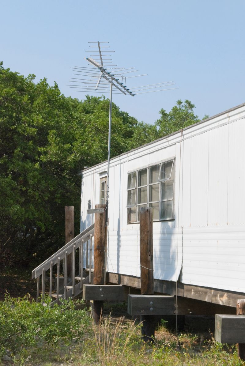 Mobile home with TV antenna, an old white house trailer in bad condition.