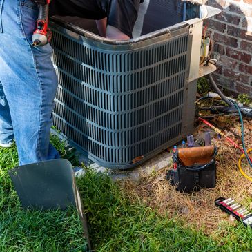 Technician repairing an outdoor air conditioning unit with tools and gauges nearby.