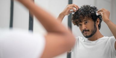 Man styling curly hair in front of a mirror.