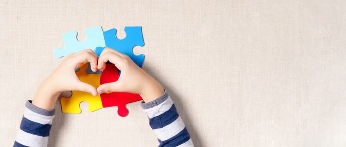 Child forming a heart shape with hands over colorful puzzle pieces, symbolizing compassionate therapy and special needs empowerment.