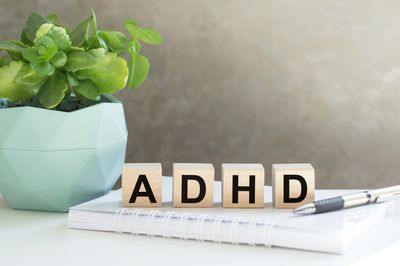 Wooden blocks spell ADHD on a notebook next to a green plant and pen.