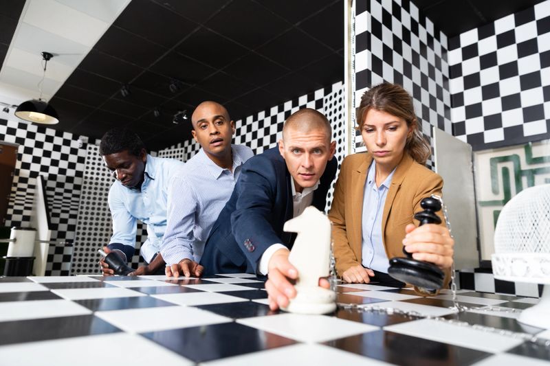 Multiracial people trying to find solution of conundrum in chess escape room