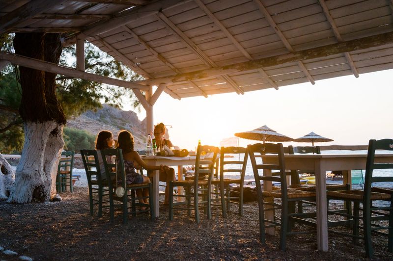 Family enjoying dinner in a restaurant on the beach at sunset. People in a cafe on a beautiful beach tavern with sunset view of the Sfinari beach in Crete, Greece.