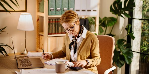 Woman working at desk using calculator and notebook.