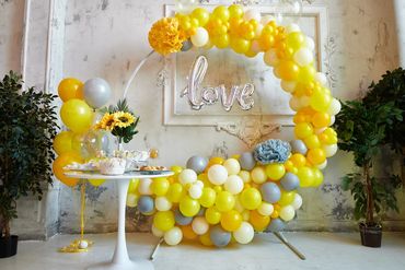 Yellow and gray balloon arch with a love sign and decorated table.