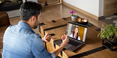 Man has a video call with a woman on a laptop at a wooden table.