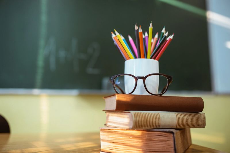 A pile of books, eyeglasses and cup filled with pencils creating anthropomorphic form.