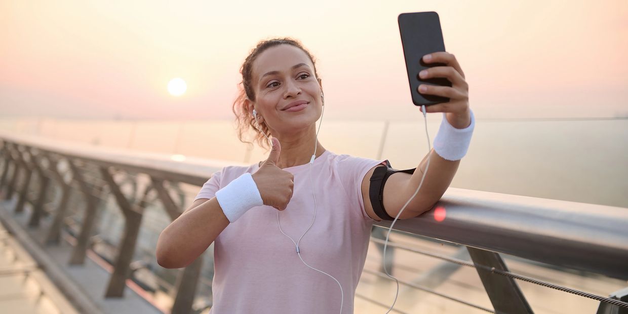 Woman in sportswear taking a selfie with a thumbs-up gesture at sunset.