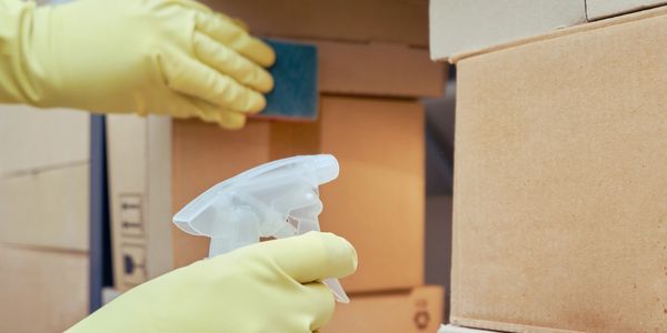 Person wearing yellow gloves cleaning cardboard boxes with spray and sponge.