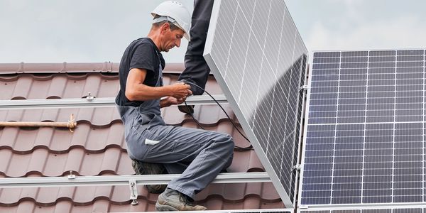 Two workers install solar panels on a rooftop under a cloudy sky.