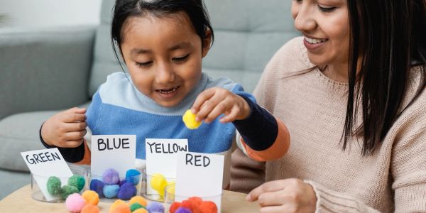 Child sorting colored pom-poms with adult's help.