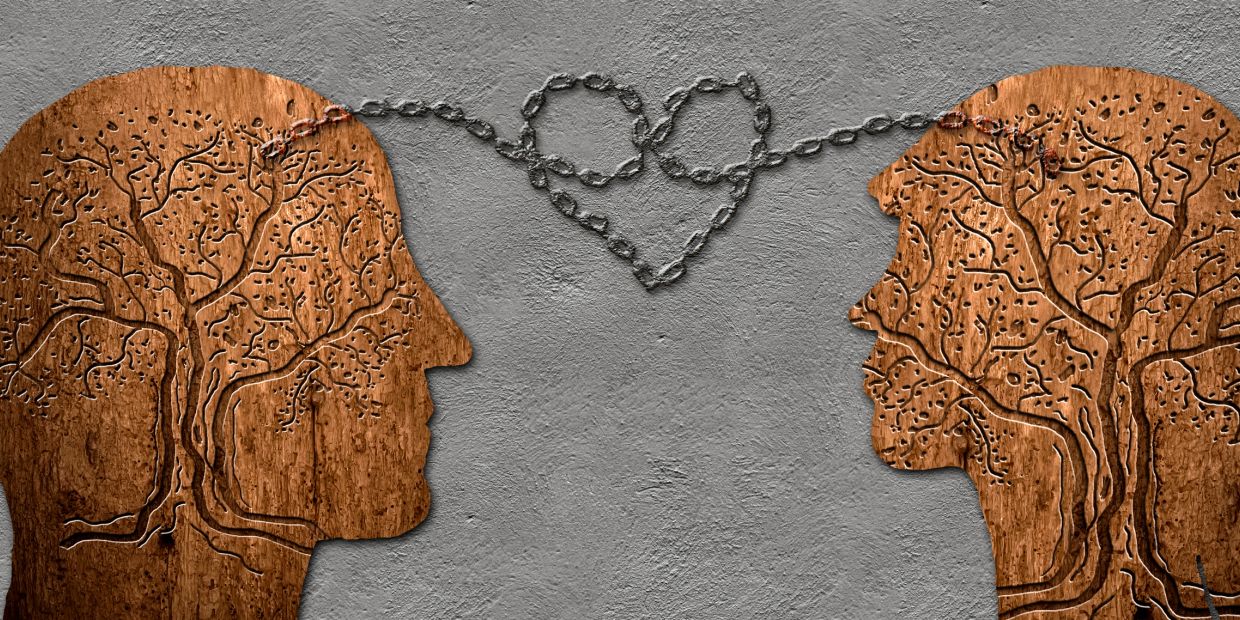 Two wooden head profiles linked by a chain forming a heart.