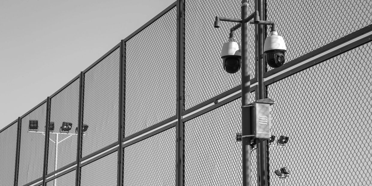 Security cameras mounted on a fence under a clear sky.