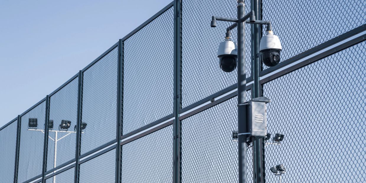 Security cameras mounted on a fence under a clear sky.