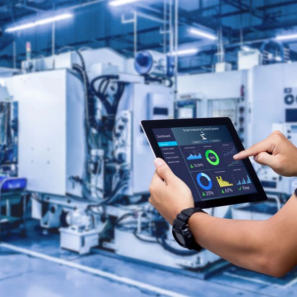 Person using a tablet to monitor smart industrial control system in a factory.