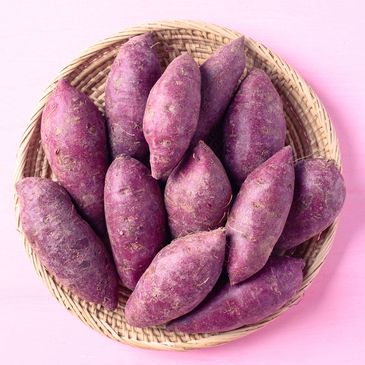 A basket filled with purple sweet potatoes on a pink background.