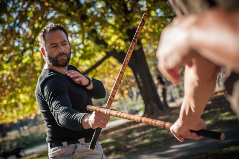 Escrima and kapap instructor demonstrates sticks fighting techniques and training methods in public park. Filipino Martial Arts. Eskrima. Kali