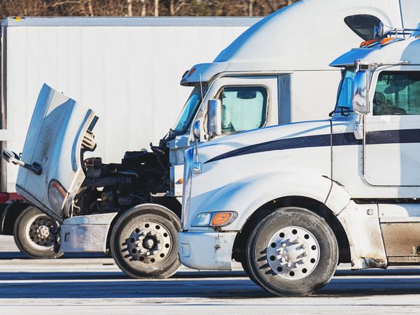 Two white semi trucks parked, one with its hood open revealing the engine.
